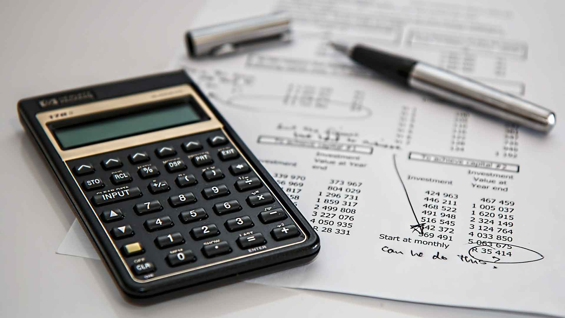 Imagens com uma folha com cálculos sobre investimentos, uma caneta e uma calculadora.
