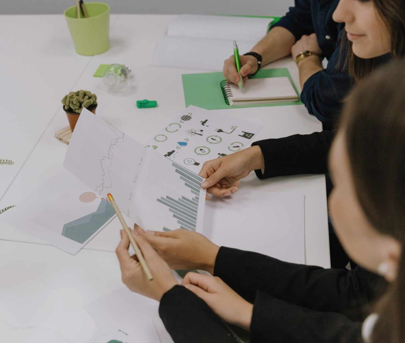 Equipa em reunião a analisar gráficos e indicadores relacionados com sustentabilidade, com documentos, apontamentos e elementos em tons de verde sobre a mesa.