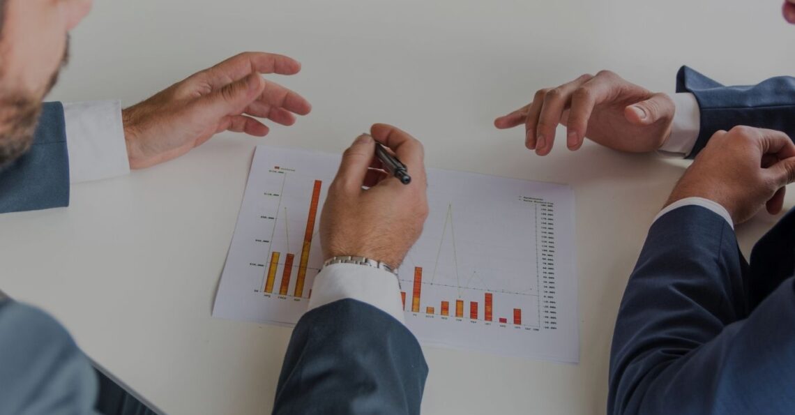 Duas pessoas a analisar gráficos de desempenho sobre uma mesa, num contexto de tomada de decisão.